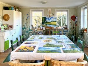 Blick in ein Künstleratelier mit einem großen Tisch in der Mitte, auf dem viele Bilder liegen.
