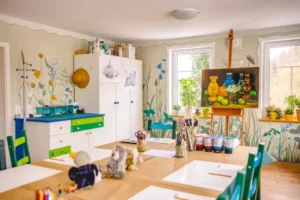 Blick in einen kunstvoll gestalteten Raum mit einer Staffelei im Hintergrund und einem für einen Malkurs vorbereiteten großen Tisch