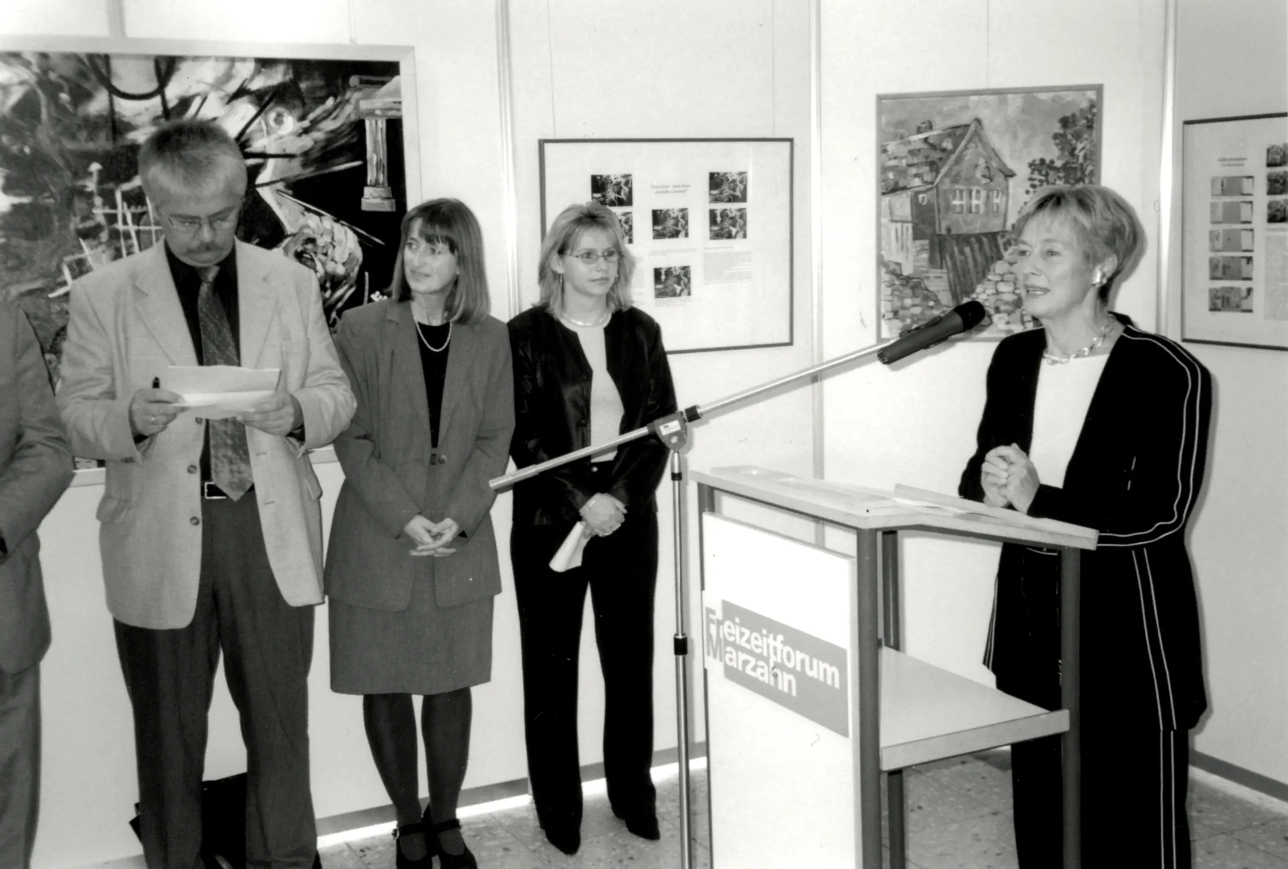 Das Bild zeigt von links nach rechts: MdB Reinhold Strobl, Evi Steiner-Böhm und Roswitha Braun-Sauerstein vor Bildern der Ausstellung „Ost-West-Dialog“ und rechts am Rednerpult die ehemalige Familienministerin Dr. Christine Bergmann.