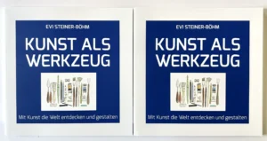 Zwei nebeneinander liegende Buchcover mit dem Titel „KUNST ALS WERKZEUG“ von Evi Steiner-Böhm auf dunkelblauem Grund. Unter dem Titel befindet sich eine Illustration verschiedener Mal- und Zeichenwerkzeuge,